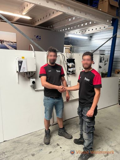 Twee mannen schudden elkaar de hand in een werkomgeving met apparatuur op de achtergrond.