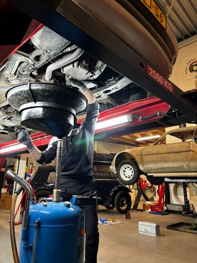 Een monteur werkt onder een auto met gereedschap in een werkplaats.