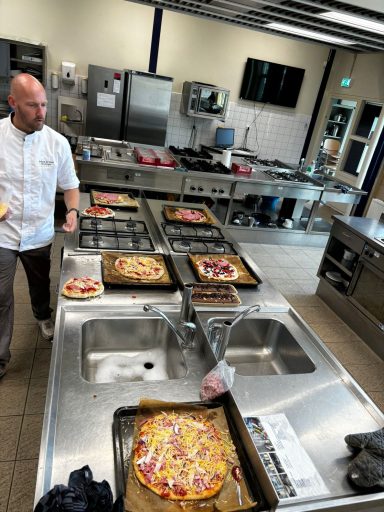 Kok bereidt meerdere pizza's in een professionele keuken.