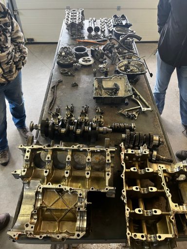 Detail van uit elkaar gearceerde motoronderdelen op een tafel.