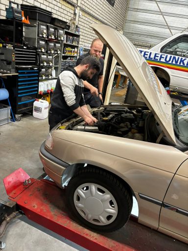 Twee mannen werken aan de motor van een auto in een garage.