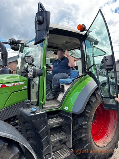 Boer zit in een groene tractor met open deur, hand omhoog.