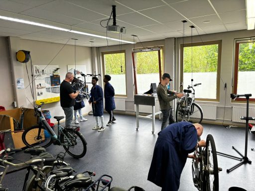Fietsreparatieworkshop met mensen die aan fietsen werken en leren.