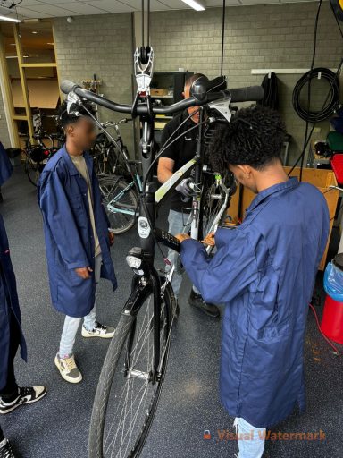 Drie jongeren in blauwe overalls repareren een fiets in een werkplaats.