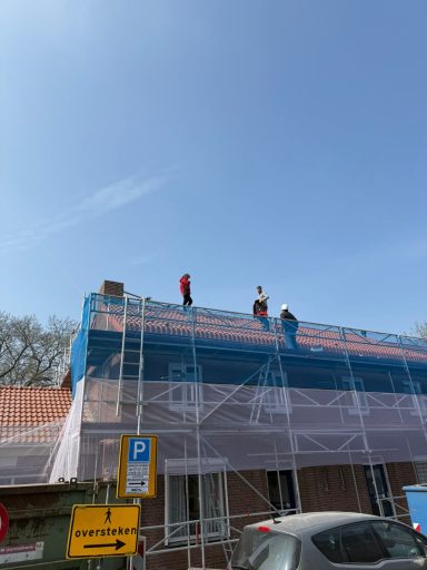 Werknemers op een dak, omgeven door steigers en een blauwe lucht.